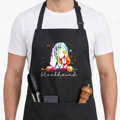 Bloodhound tie-dye apron - Watercolor bloodhound head and paws with rainbow splatters and white script text — shown on a black cotton canvas apron against a white background