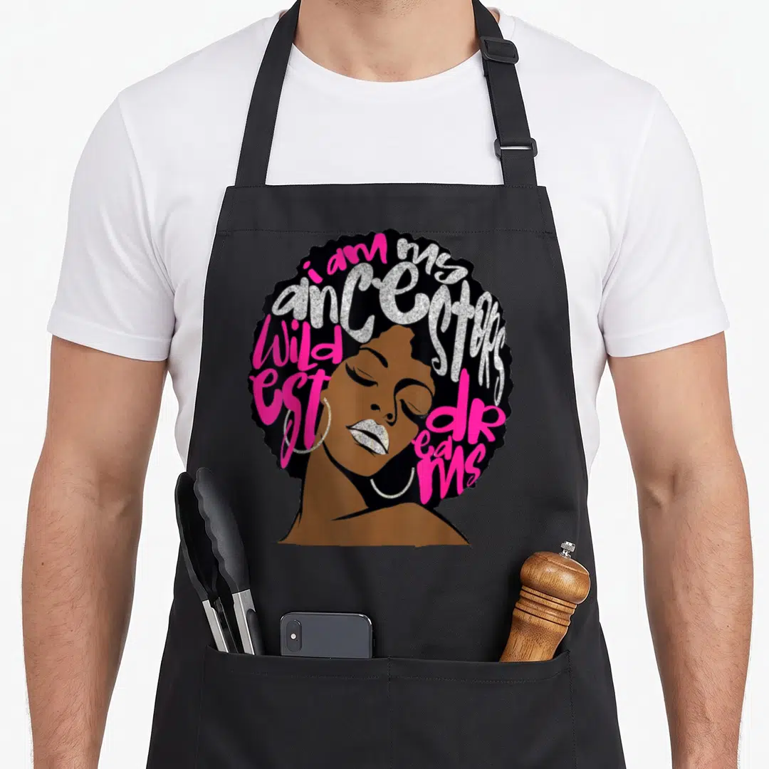 Queen pride apron - Woman with afro containing text i am my ancestors wildest dreams in pink and silver — shown on a black cotton canvas apron against a white background