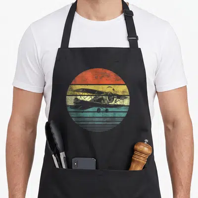 Aviator pilot airplane apron - Grey biplane silhouette over orange, yellow, teal, and grey horizontal stripes — shown on a black cotton canvas apron against a white background