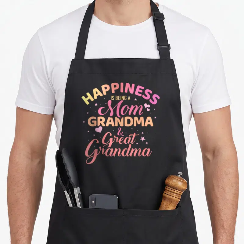 Funny happiness grandma apron - Stacked text reading HAPPINESS IS BEING A Mom GRANDMA & Great Grandma with stars — shown on a black cotton canvas apron against a white background