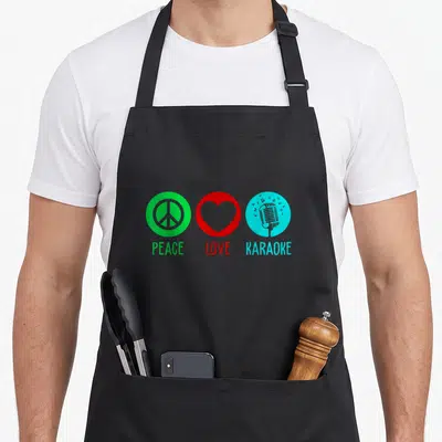 Singing karaoke apron - Three colored circles with peace sign, heart, and microphone above matching text — shown on a black cotton canvas apron against a white background