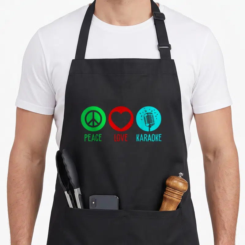 Singing karaoke apron - Three colored circles with peace sign, heart, and microphone above matching text — shown on a black cotton canvas apron against a white background