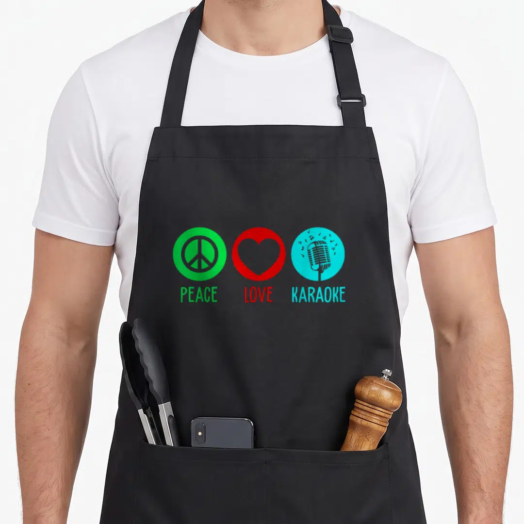 Singing karaoke apron - Three colored circles with peace sign, heart, and microphone above matching text — shown on a black cotton canvas apron against a white background
