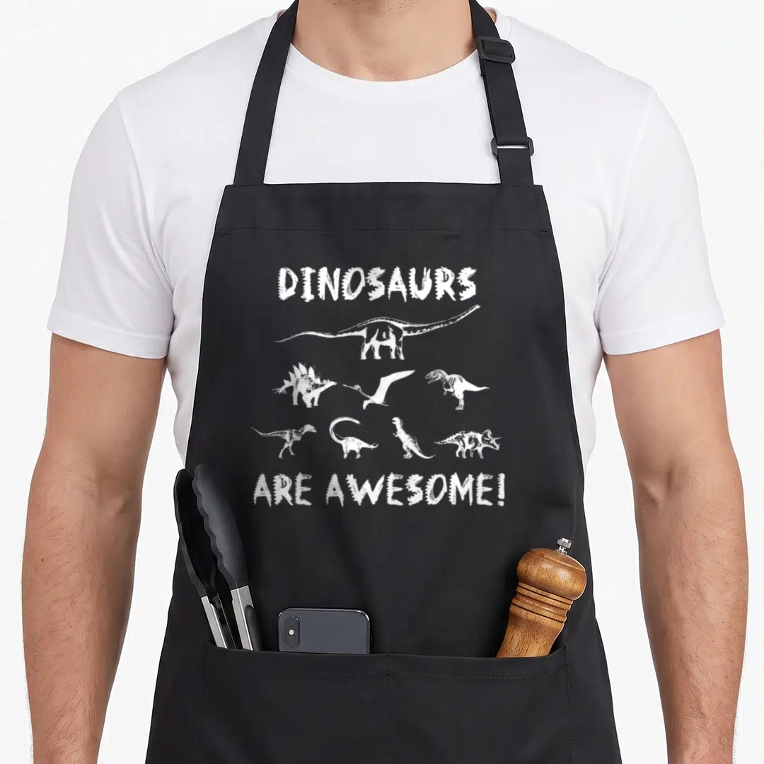 Vintage dino dinosaur apron - White distressed DINOSAURS ARE AWESOME! text with seven dinosaur silhouettes arranged — shown on a black cotton canvas apron against a white background