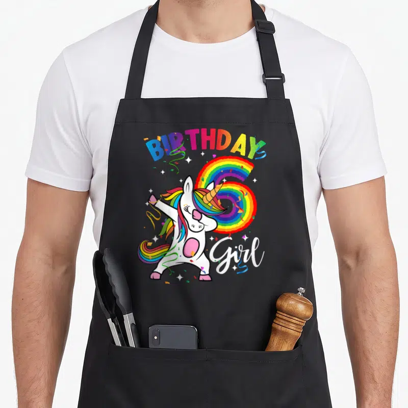 Gif birthday apron - Cartoon unicorn dabbing over rainbow number 6 with BIRTHDAY Girl text — shown on a black cotton canvas apron against a white background