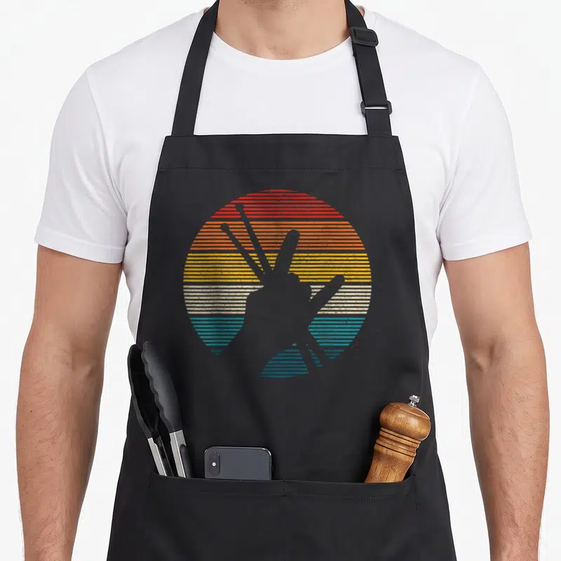 Drummer horn apron - Retro circular sunset with horizontal stripes in red orange yellow white and blue featuring two — shown on a black cotton canvas apron against a white background