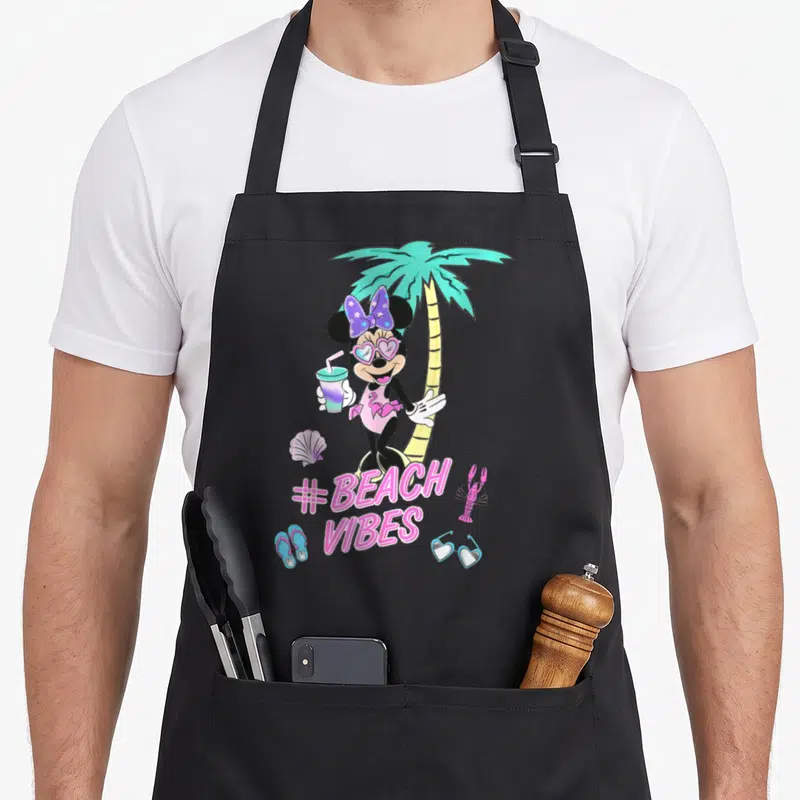 Beach unicorn apron - Minnie Mouse holding a drink near a palm tree with shell, lobster, flip flops, and #BEACH VIBES — shown on a black cotton canvas apron against a white background