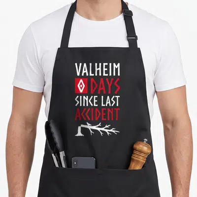 Accident norse apron - VALHEIM DAYS SINCE LAST ACCIDENT text with red square, white bird on branch — shown on a black cotton canvas apron against a white background