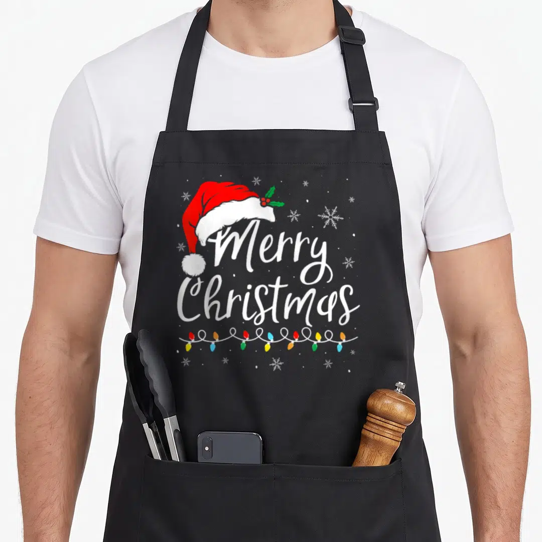 Light santa aprons - Red Santa hat with holly above white Merry Christmas text and colorful string lights — shown on a black cotton canvas apron against a white background
