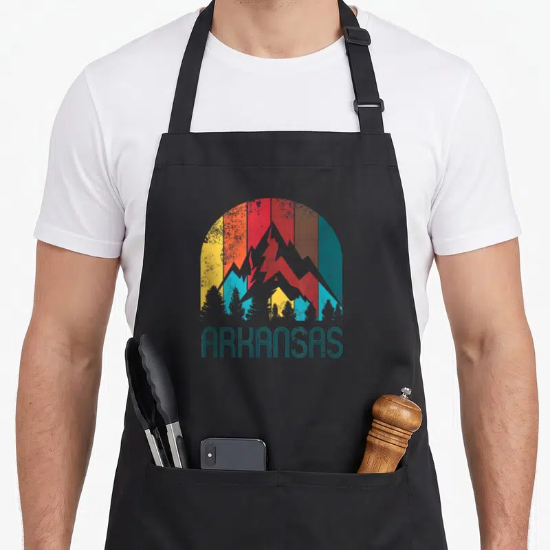 Funny arkansas apron - Retro grey mountains with teal red yellow stripes and ARKANSAS text — shown on a black cotton canvas apron against a white background