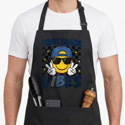 School grade boys apron - Cartoon smiley face with cap and sunglasses making peace signs over a navy and black — shown on a black cotton canvas apron against a white background