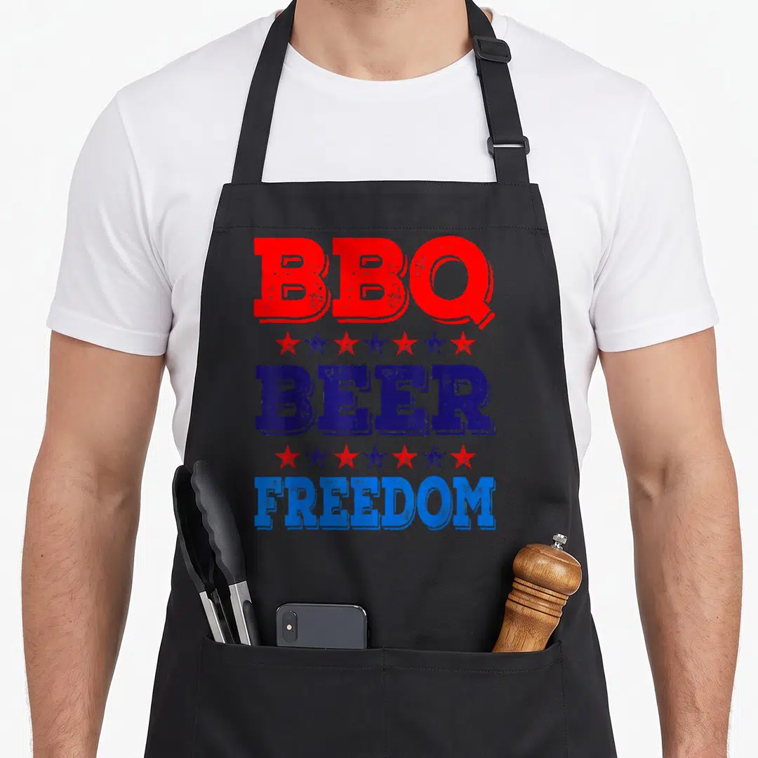 Summer 4th of july apron - Stacked red and blue text reading BBQ BEER FREEDOM separated by alternating star rows — shown on a black cotton canvas apron against a white background