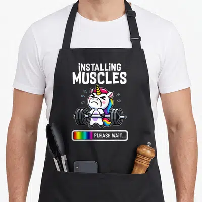 Workout unicorn apron - Cartoon unicorn lifting barbell with text installing muscles and rainbow loading bar please wait — shown on a black cotton canvas apron against a white background