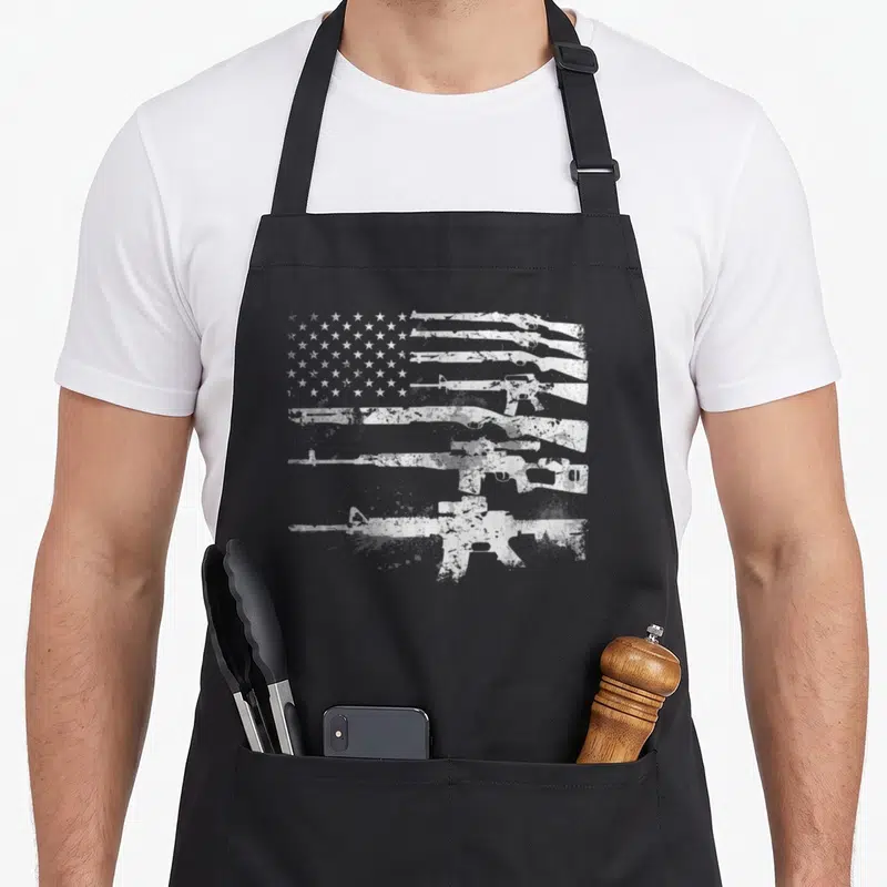 Gun machine apron - White distressed rifle silhouettes forming USA flag stripes on grey background — shown on a black cotton canvas apron against a white background