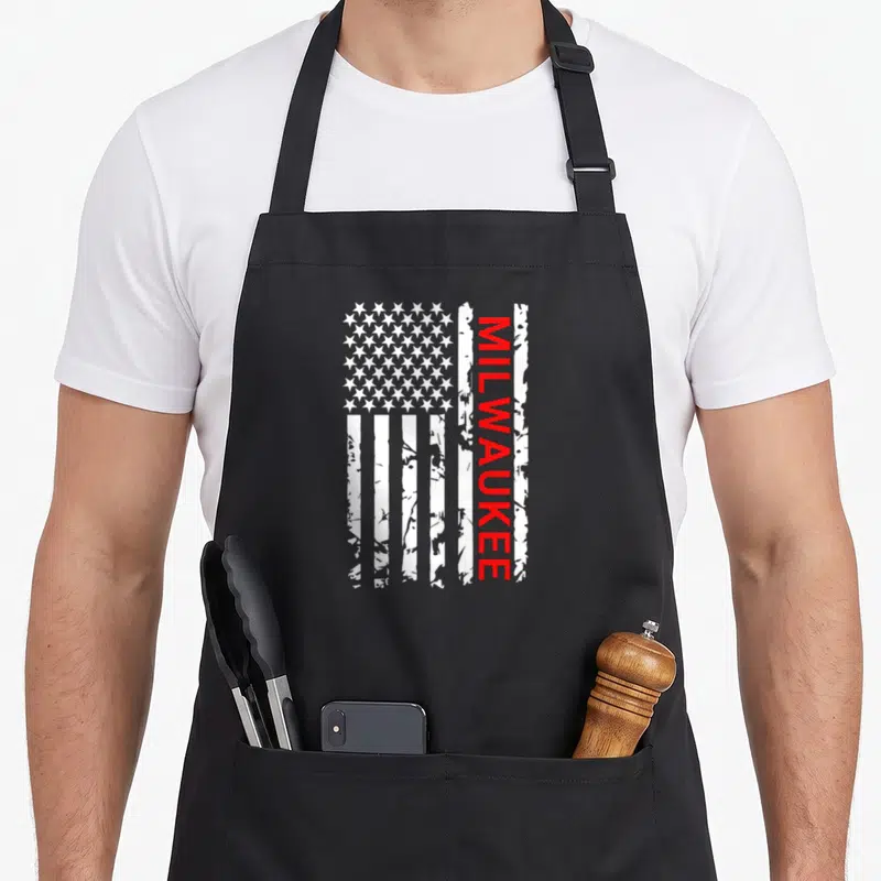 Funny flag milwaukee apron - Distressed USA flag with vertical red MILWAUKEE text on the right side — shown on a black cotton canvas apron against a white background