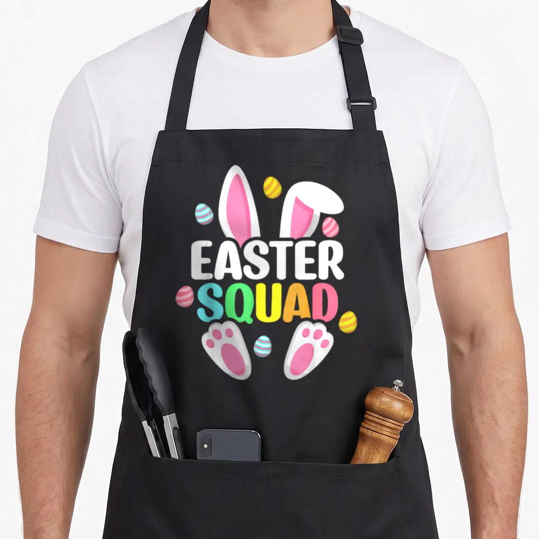 Squad easter egg apron - Cartoon bunny ears and paws framing stacked EASTER SQUAD text with six striped eggs — shown on a black cotton canvas apron against a white background