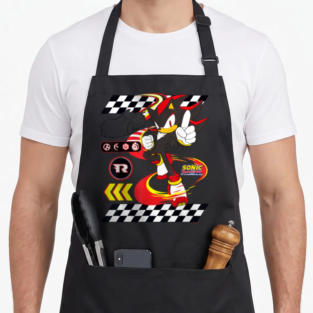 Racing ultimate apron - Shadow the Hedgehog thumbs up with Sonic Racing CrossWorlds logo, checkered flags, and racing — shown on a black cotton canvas apron against a white background