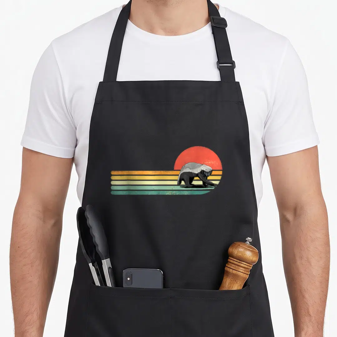 Wild honey badger apron - Retro honey badger illustration with red sun and four horizontal stripes in orange yellow — shown on a black cotton canvas apron against a white background