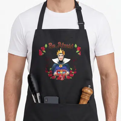 Afraid queen apron - Evil Queen holding chest with Be Afraid text and red roses framing a Snow White apple — shown on a black cotton canvas apron against a white background