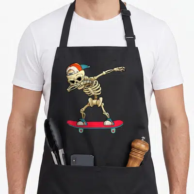 Skateboard skeleton apron - Beige cartoon skeleton dabbing on red skateboard wearing orange cap and blue sneakers — shown on a black cotton canvas apron against a white background