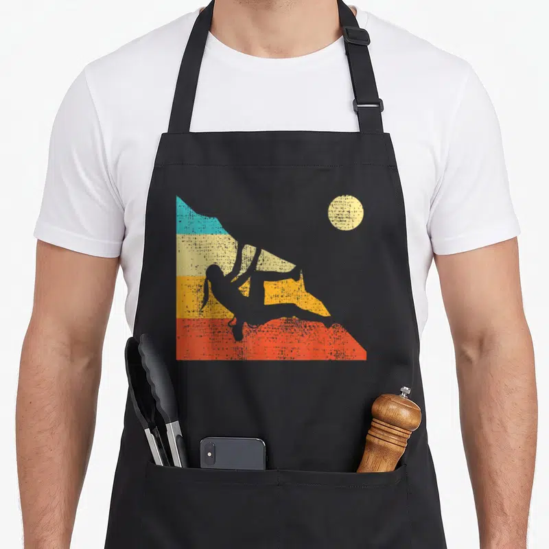 Free bouldering apron - Retro white climber silhouette against blue yellow orange and red mountain bands with beige sun — shown on a black cotton canvas apron against a white background