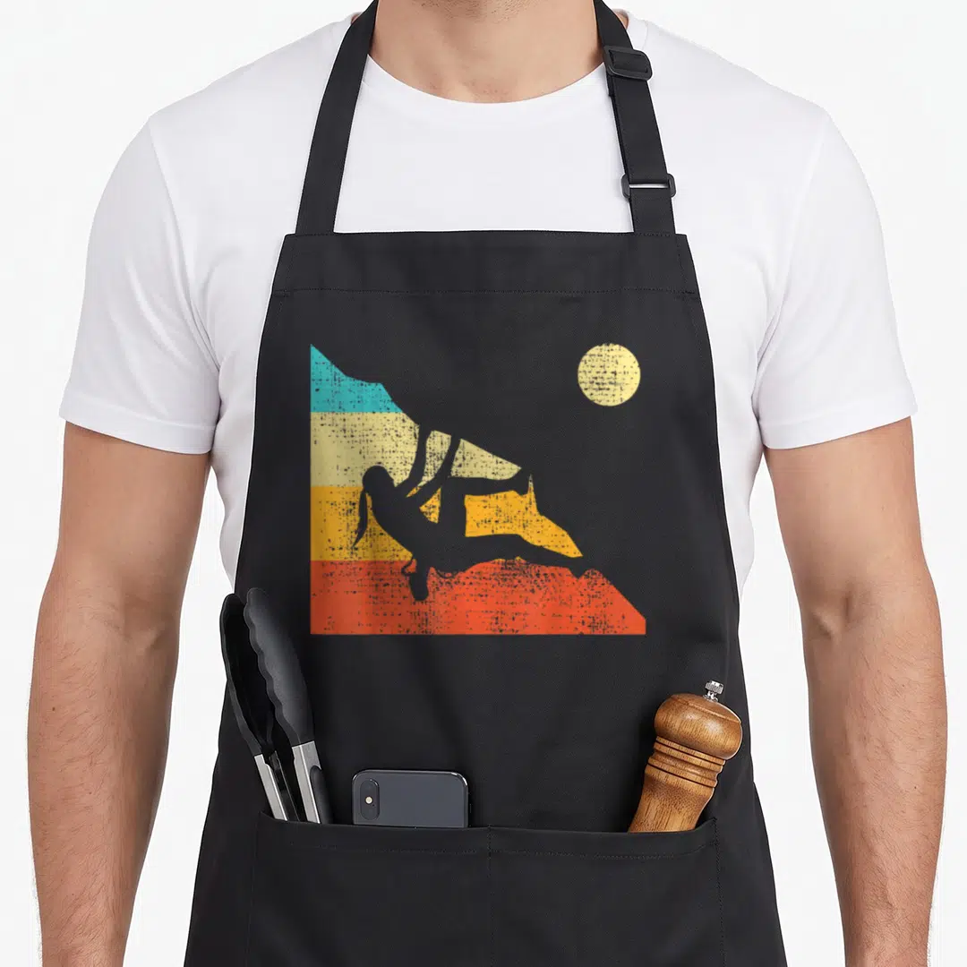 Free bouldering apron - Retro white climber silhouette against blue yellow orange and red mountain bands with beige sun — shown on a black cotton canvas apron against a white background