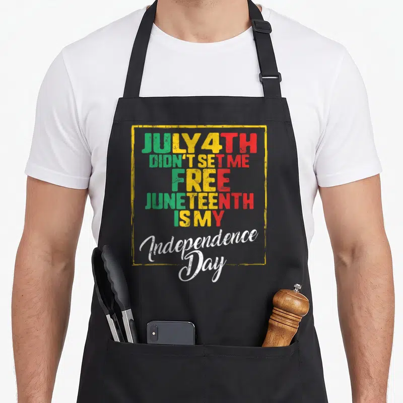 Ancestor 4th of july apron - Stacked text JULY 4TH DIDN'T SET ME FREE in green yellow red inside distressed yellow — shown on a black cotton canvas apron against a white background