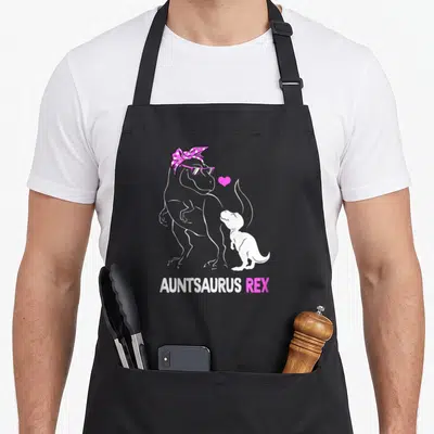 Auntie dinosaur apron - White T-Rex with pink bandana and glasses beside baby T-Rex and pink heart, Auntsaurus Rex text — shown on a black cotton canvas apron against a white background