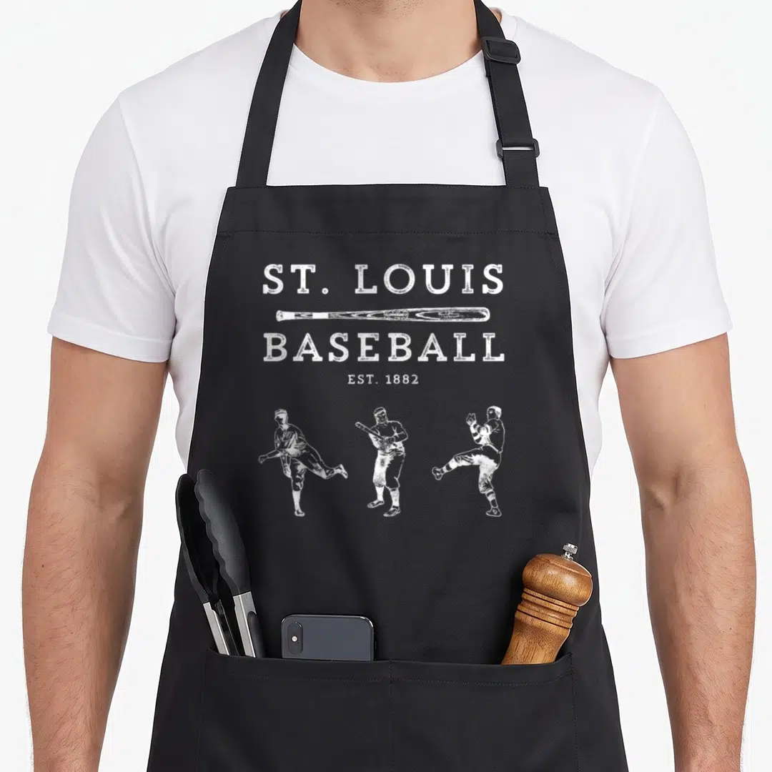 Louis baseball apron - White distressed text ST LOUIS BASEBALL EST 1882 with bat and three vintage player silhouettes — shown on a black cotton canvas apron against a white background