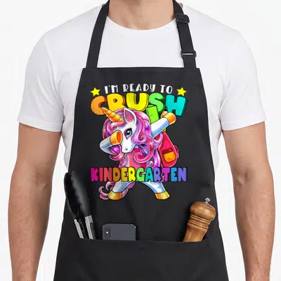 School unicorn aprons - Dabbing unicorn with pink mane, backpack, ruler, and colorful text ready to crush kindergarten — shown on a black cotton canvas apron against a white background