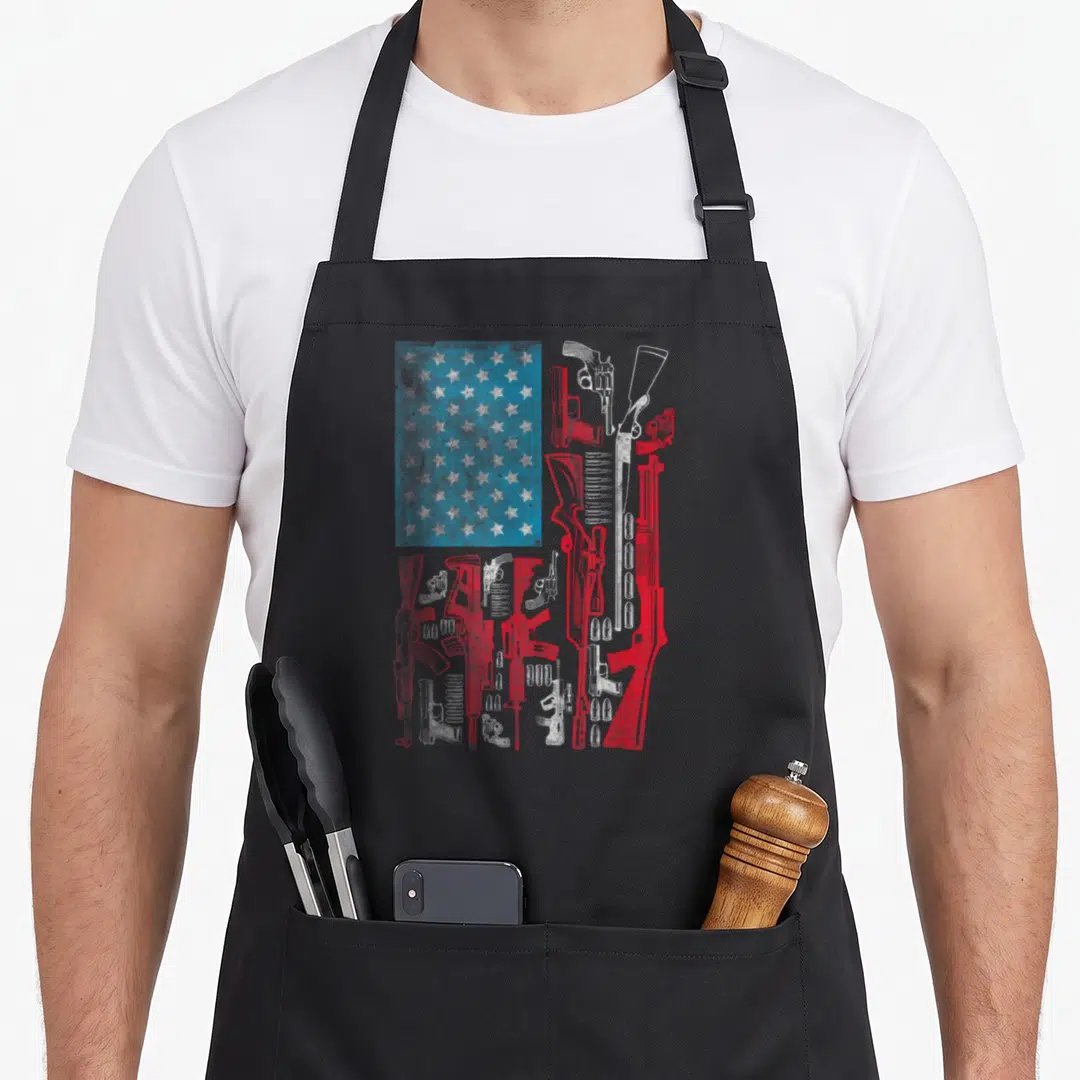 Riffle american flag apron - Red white blue guns and stars arranged as distressed US flag pattern — shown on a black cotton canvas apron against a white background