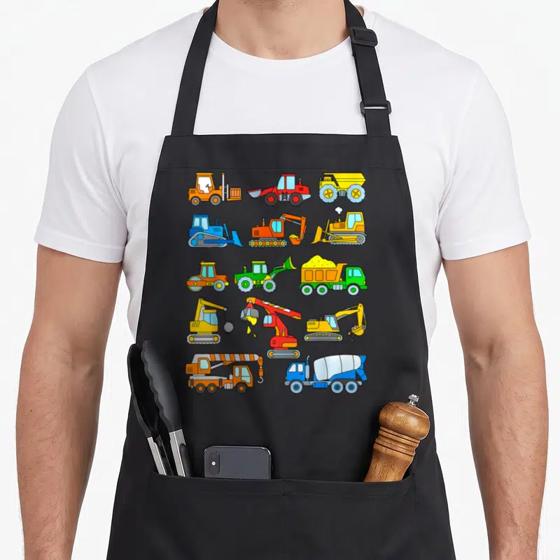 Excavator construction apron - Grid of 13 cartoon construction vehicles in yellow orange blue red and green — shown on a black cotton canvas apron against a white background