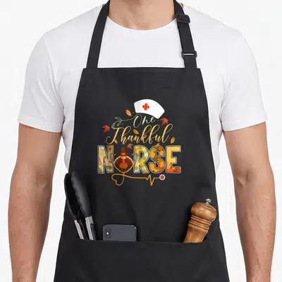 Nurse thankful apron - One Thankful NURSE text with turkey, nurse hat, and stethoscope in fall colors — shown on a black cotton canvas apron against a white background