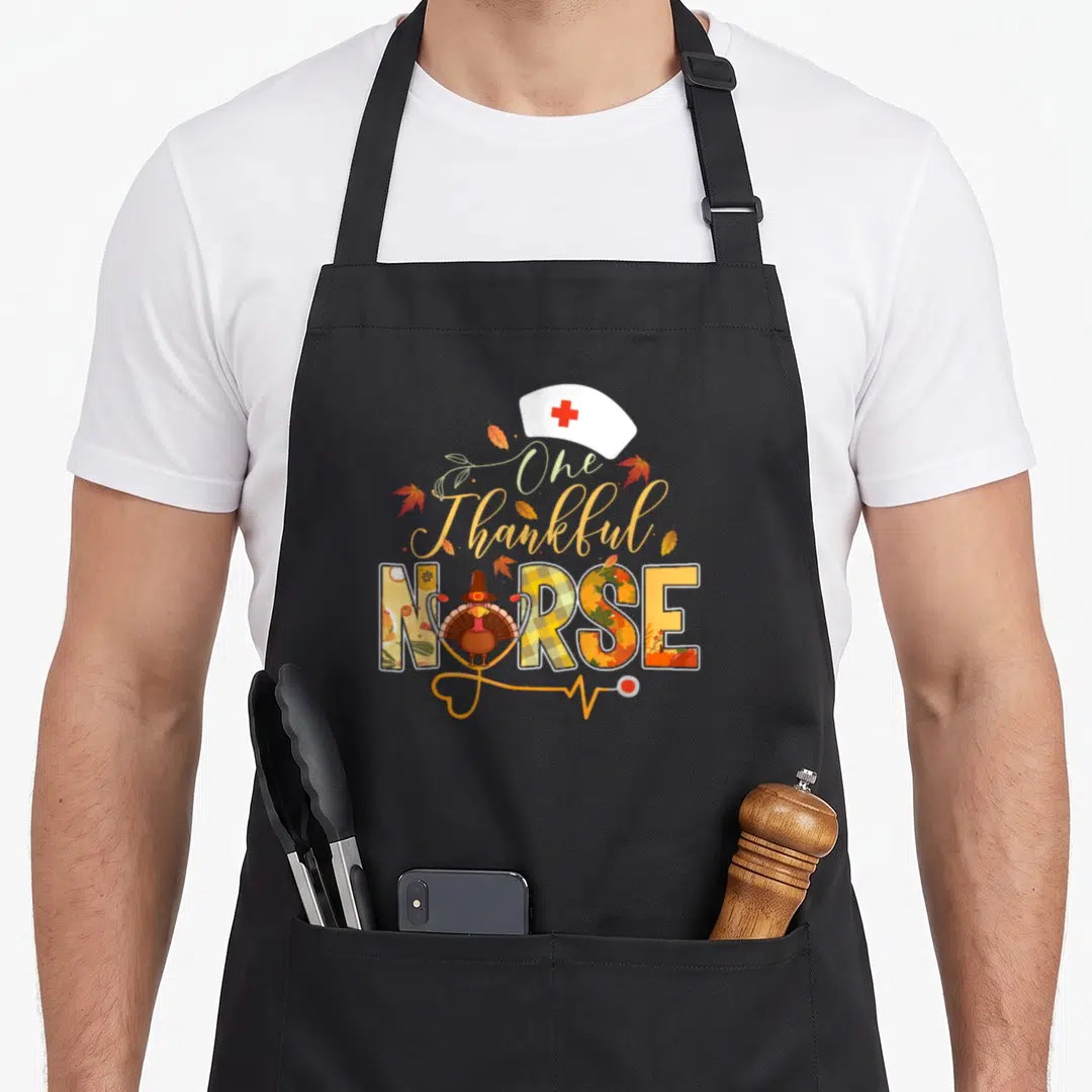 Nurse thankful apron - One Thankful NURSE text with turkey, nurse hat, and stethoscope in fall colors — shown on a black cotton canvas apron against a white background