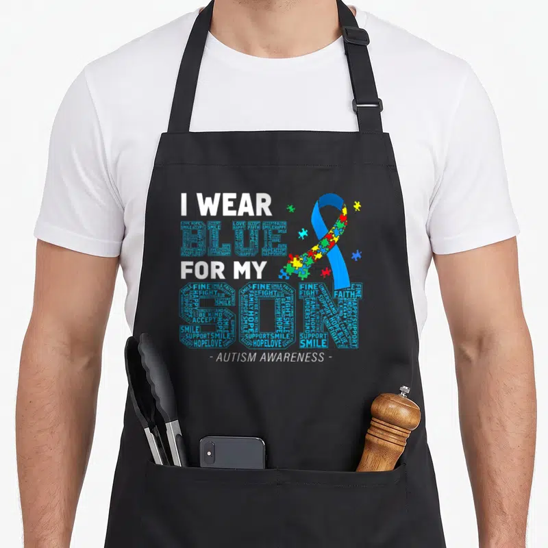 Parent dad and son aprons - I WEAR BLUE FOR MY SON text with colorful puzzle piece ribbon — shown on a black cotton canvas apron against a white background