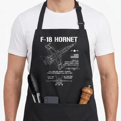 Fighter airplane apron - White F-18 Hornet line art with length, speed, and wingspan foldable specs next to US flag — shown on a black cotton canvas apron against a white background