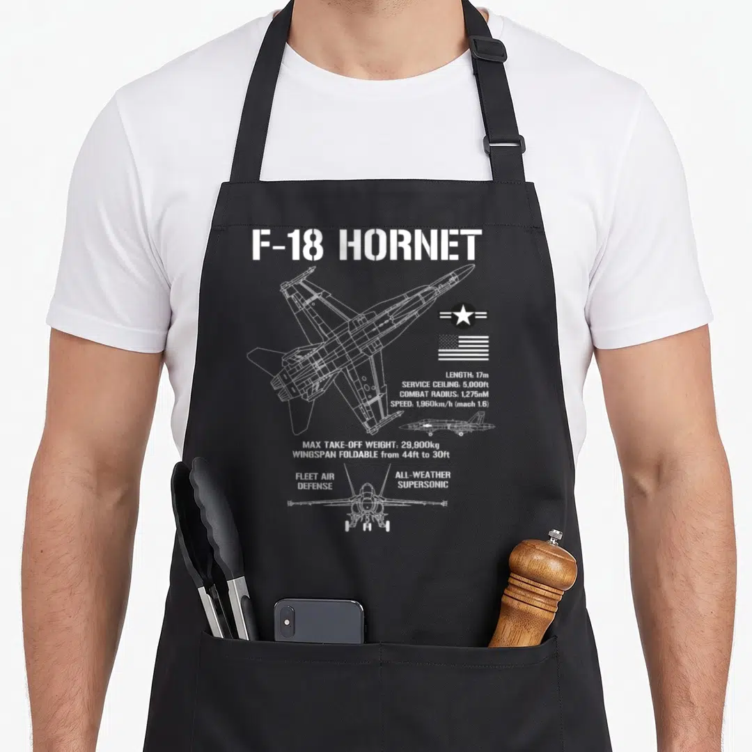 Fighter airplane apron - White F-18 Hornet line art with length, speed, and wingspan foldable specs next to US flag — shown on a black cotton canvas apron against a white background