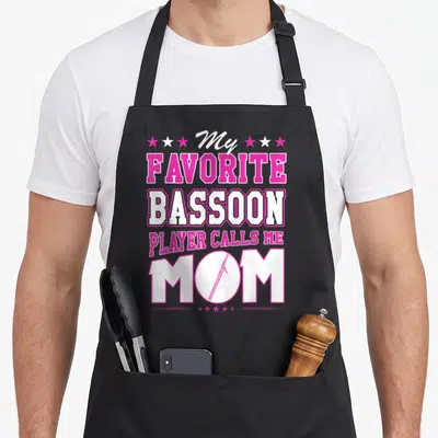Player call bassoon apron - Pink and white text My Favorite Bassoon Player Calls Me Mom with bassoon inside O — shown on a black cotton canvas apron against a white background