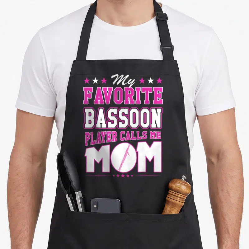 Player call bassoon apron - Pink and white text My Favorite Bassoon Player Calls Me Mom with bassoon inside O — shown on a black cotton canvas apron against a white background