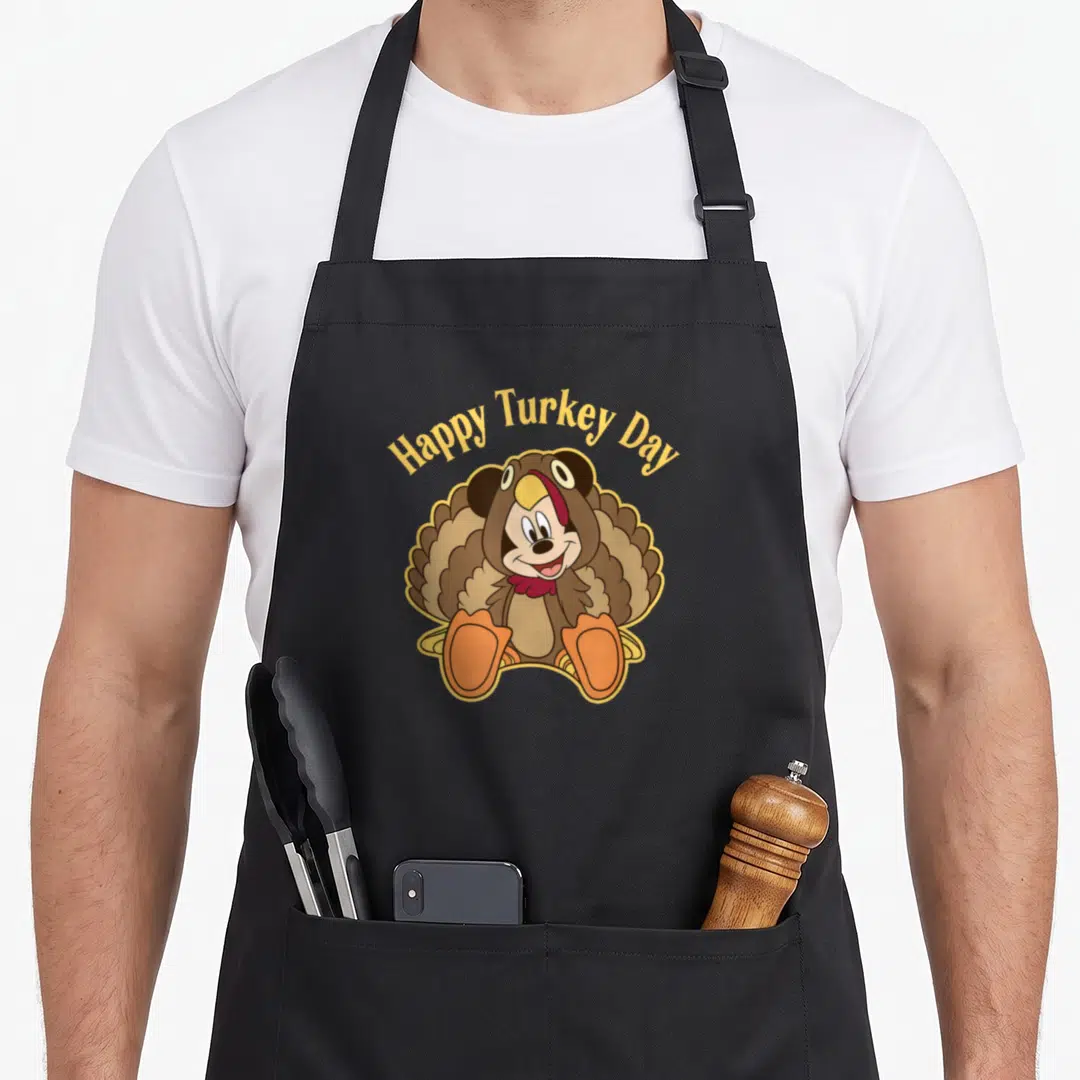 Friend turkey apron - Mickey Mouse wearing a brown turkey costume with Happy Turkey Day text in yellow — shown on a black cotton canvas apron against a white background