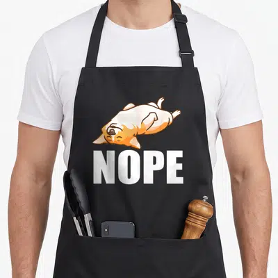 Lazy corgi apron - Cartoon dog lying on back with white nope text below — shown on a black cotton canvas apron against a white background
