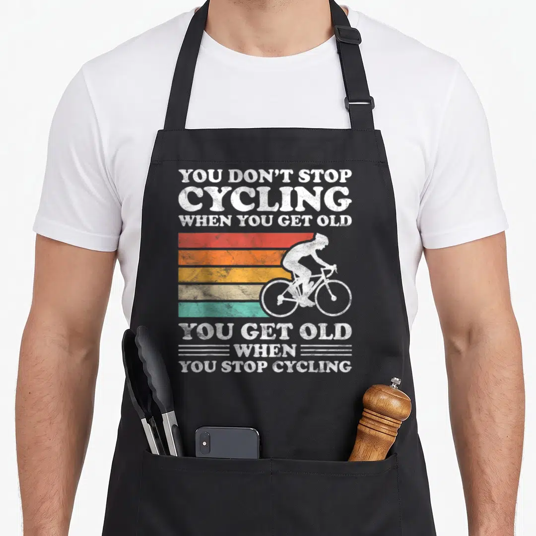 Cycling grandpa apron - Retro cyclist silhouette on red orange yellow teal stripes with text about not stopping cycling — shown on a black cotton canvas apron against a white background