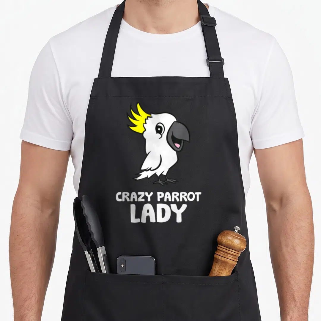Cockatoo crazy parrot lady apron - Cartoon white parrot with yellow crest above stacked text CRAZY PARROT LADY — shown on a black cotton canvas apron against a white background