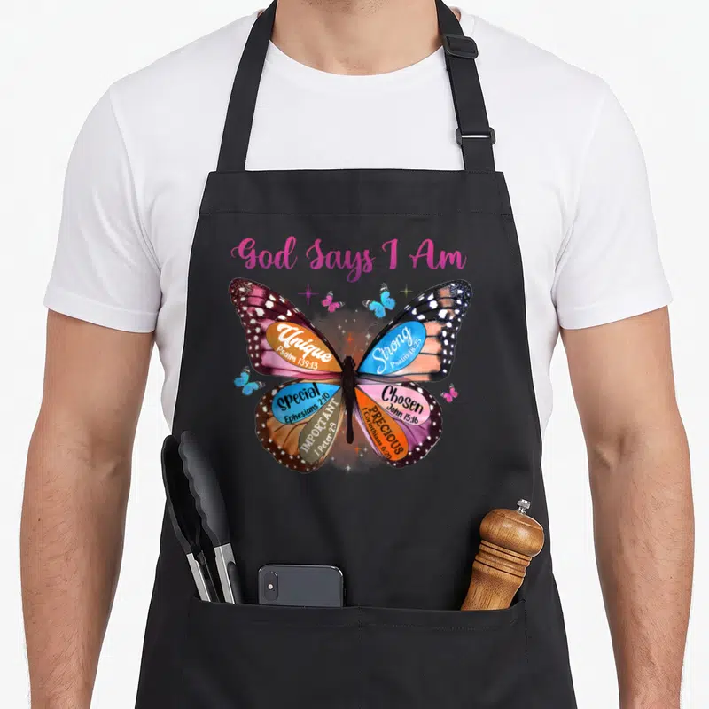 Verse god says i am apron - Realistic butterfly with pink blue orange brown wings containing scripture verses like — shown on a black cotton canvas apron against a white background