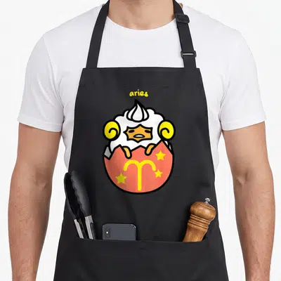 Gudetama aries kitchen apron - Cartoon ram hatching from red egg with aries text and three yellow stars — shown on a black cotton canvas apron against a white background