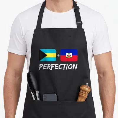 Bahamian heritage aprons - Two flags with plus sign and white PERFECTION text below — shown on a black cotton canvas apron against a white background
