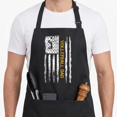 Volleyball american flag apron - Distressed US flag with yellow vertical text and jumping player silhouette — shown on a black cotton canvas apron against a white background
