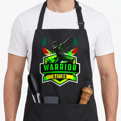 Cpl patriotic apron - Cartoon cricketer swinging bat above WARRIOR NATION shield with green red yellow flag — shown on a black cotton canvas apron against a white background
