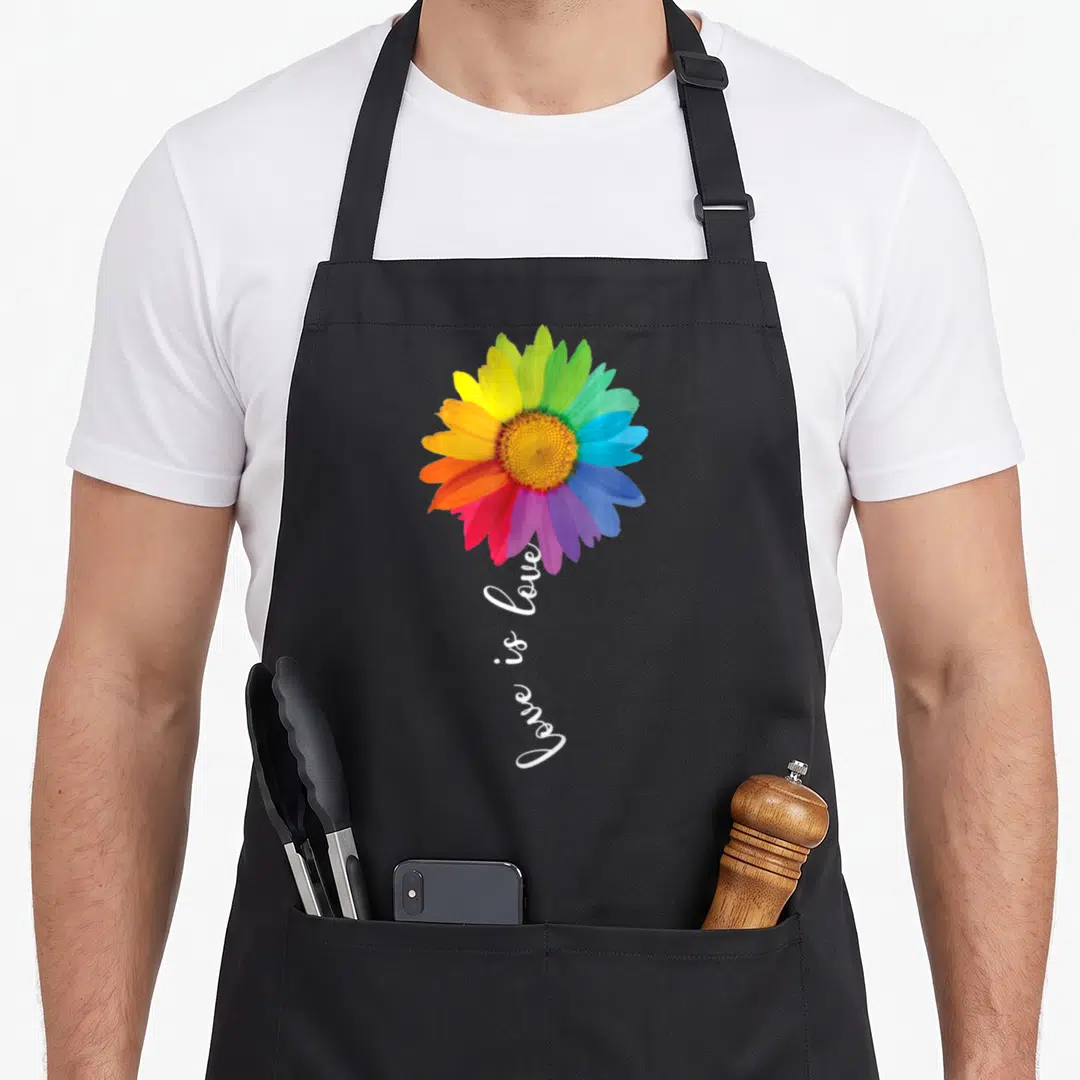 Lgbt sunflower apron - Rainbow flower with vertical love is love script on black background — shown on a black cotton canvas apron against a white background