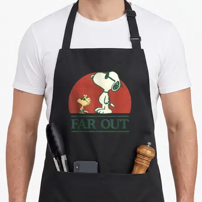 Far decade apron - Snoopy and Woodstock cartoon with FAR OUT text on red circle background — shown on a black cotton canvas apron against a white background